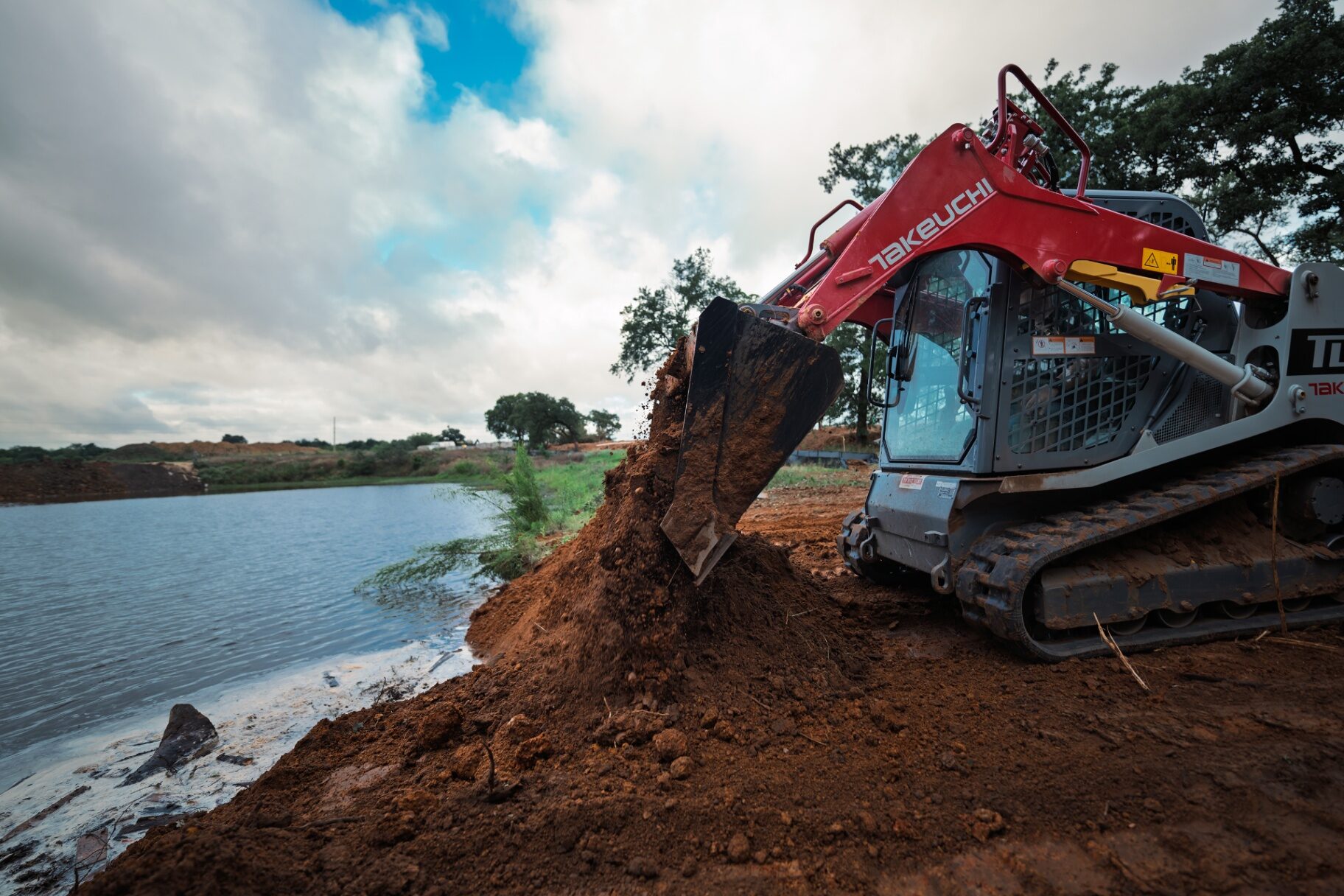 Takeuchi track loader excavating near a pond bank