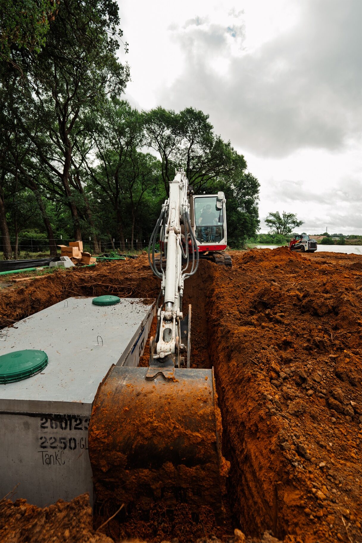 Excavator trenching beside a concrete septic tank